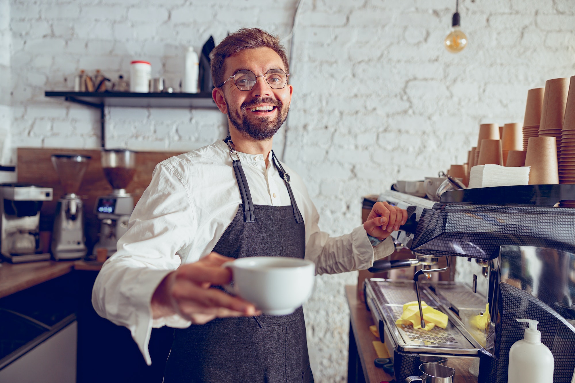 Cheerful male barista offering coffee in cafe
